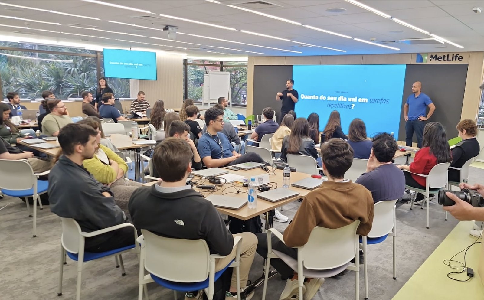 Sala cheia na MetLife durante a abertura do Hackathon de Implementação, com a pergunta sobre tarefas repetitivas no telão